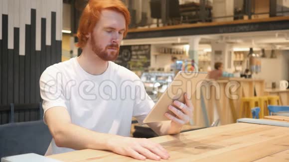 震惊好奇红发胡子男子使用平板电脑在咖啡厅视频的预览图
