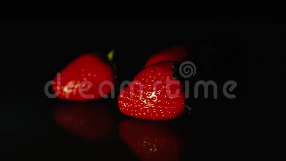 三颗草莓美丽地躺在黑色的桌子上黑色的背景在一缕光线下高清高清视频的预览图