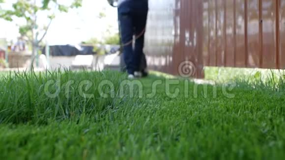 前景绿草如茵一个人带着割草机在后台移动低角度拍摄视频的预览图