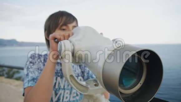 一个十五岁的少年从高高的高架上看着海岸进入望远镜的特写镜头视频的预览图