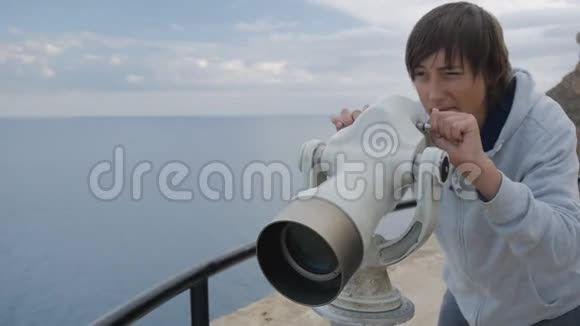 十五岁的男孩穿着灰色连帽衫从高高的观景台上望着大海进入望远镜视频的预览图