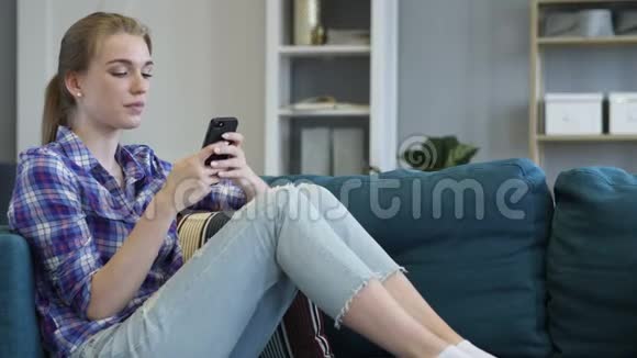 年轻女性在沙发上放松时使用智能手机视频的预览图