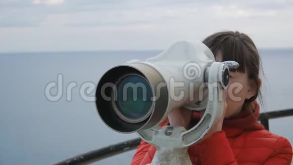 一位穿着红色泡泡夹克的年轻女子从海面上的观察台上近距离观察望远镜视频的预览图