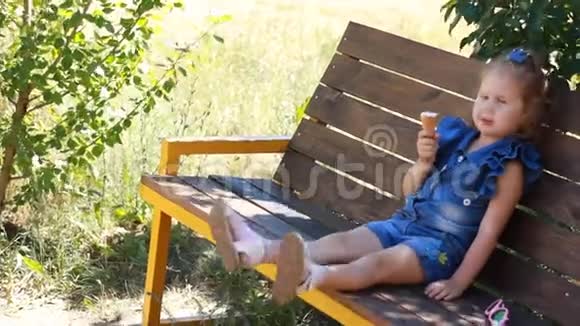 小女孩正坐在公园的长凳上吃冰淇淋视频的预览图