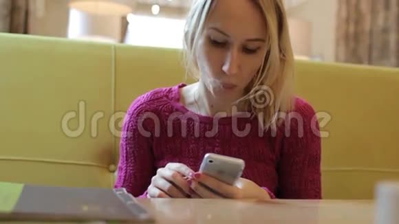 年轻快乐的金发女郎用手机在咖啡馆喝茶视频的预览图