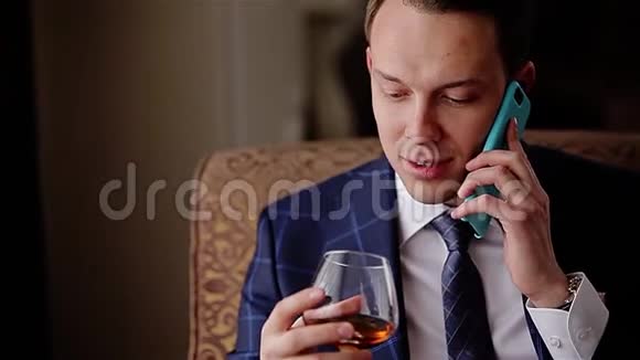 年轻时尚的年轻人拿着一杯威士忌在电话里说话看着玻璃视频的预览图