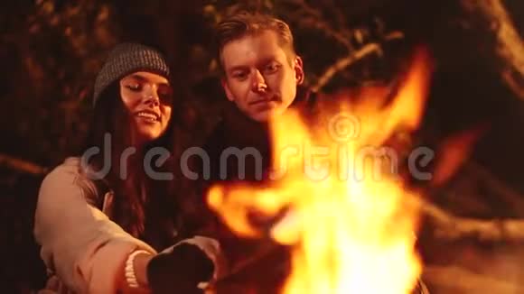 快乐的一对夫妇微笑着在夜间海滩篝火上烤棉花糖视频的预览图