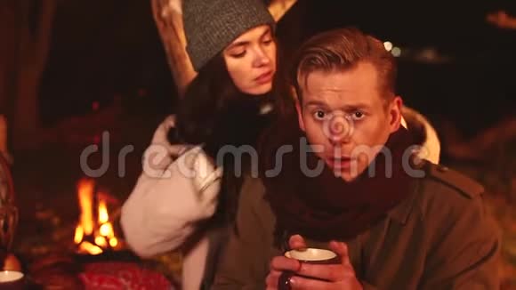女孩照顾生病的男人红鼻子他们在外面的秋天公园黄昏喝热茶附近篝火高清视频的预览图