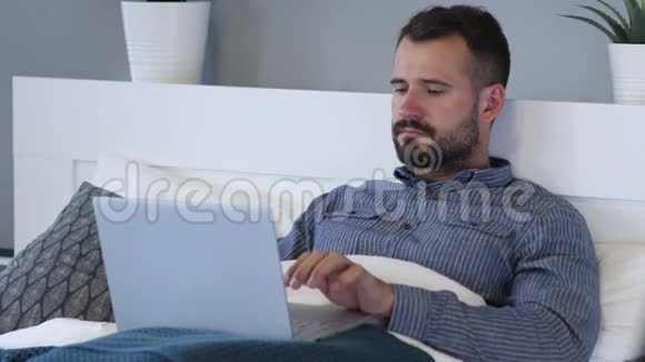 快乐男人在床上使用笔记本电脑的成功反应视频的预览图