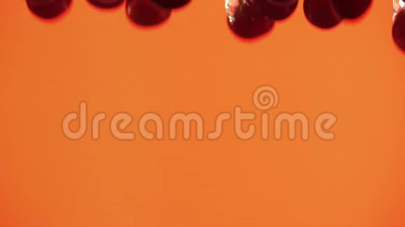 在橙色背景下将成熟的樱桃倒入水中液态红色浆果视频的预览图