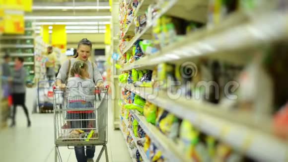 女人和女孩在超市选择产品妈妈和女儿把一些东西放在篮子里后沿着货架走视频的预览图