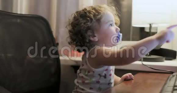 小女孩卷发嘴里放着奶嘴坐在电脑显示器旁边视频的预览图