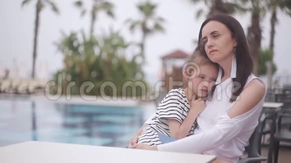 妈妈和伤心的女儿坐在泳池边的桌子旁视频的预览图