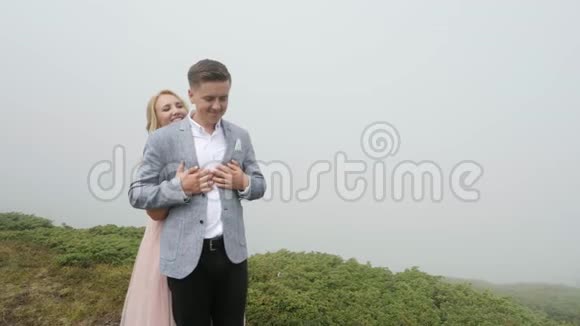 在雾的背景下一对豪华夫妇在山上的草地上散步视频的预览图