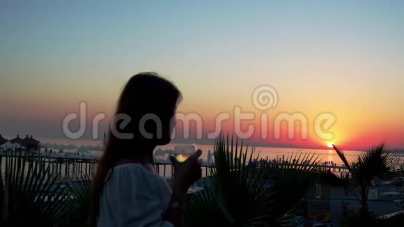 日落时海边的一个漂亮女孩喝着一杯酒4K视频的预览图