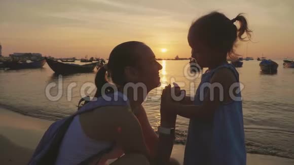 日落时年轻母亲和她的小女儿在海滩上的温柔肖像视频的预览图