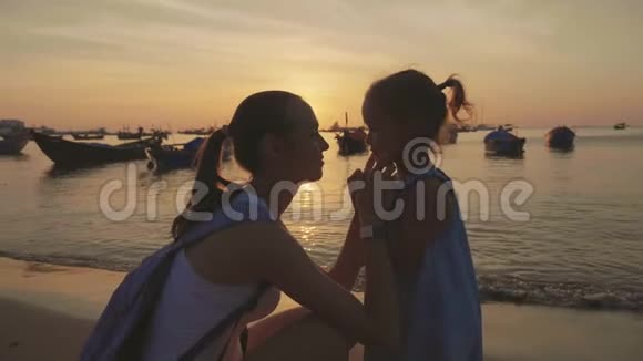 日落时年轻母亲和她的小女儿在海滩上的温柔肖像视频的预览图