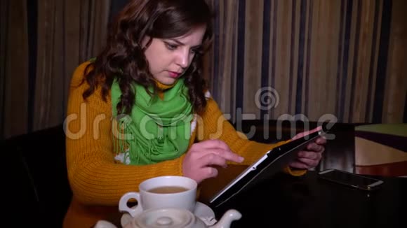 年轻漂亮的女孩坐在桌边的咖啡馆里用平板电脑她微笑着特写镜头绿色的布鲁内特视频的预览图