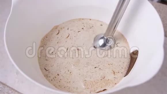 将液体黑巧克力和奶油混合在一个白色的碗和搅拌机中特写镜头视频的预览图