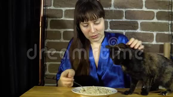 一个女人坐在一张桌子旁吃燕麦片旁边是一只猫视频的预览图