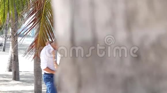 年轻的幸福夫妇在棕榈树叶下拥抱和亲吻浪漫关系或旅行概念高清高清视频的预览图