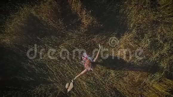 空中飞行迷人的女孩在草地上旋转拿着一顶草帽从上面看慢动作视频的预览图