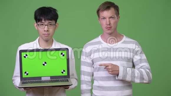 两个年轻的多民族商人用手指着相机展示笔记本电脑视频的预览图