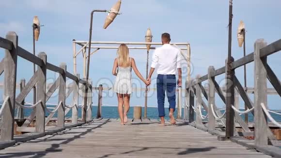 年轻的幸福夫妇在蓝天背景上的木墩上行走浪漫的概念高清1920x1080视频的预览图