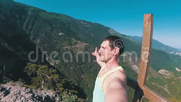 在一座岩石山的山顶上一个人带着十字架的微笑喜悦和旋转的相机视频的预览图