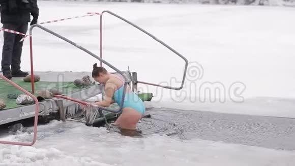 一个年轻的女孩沉浸在冰洞里在寒冷的河流里硬化和游泳健康生活方式视频的预览图