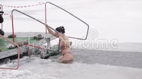 一个年轻的女孩沉浸在冰洞里在寒冷的河流里硬化和游泳健康生活方式视频的预览图