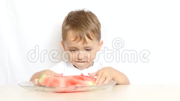 男孩坐在桌子旁高兴地在白色的背景上吃西瓜视频的预览图