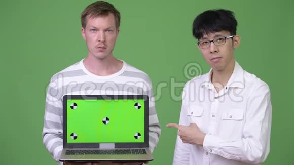 两个年轻的多民族商人用手指着相机展示笔记本电脑视频的预览图