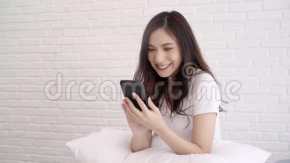 慢动作美丽的亚洲妇女使用智能手机而躺在床上在她的卧室视频的预览图