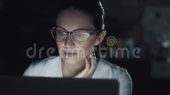 在黑暗中在电脑前工作的年轻女子带眼镜的监视器的反射视频的预览图