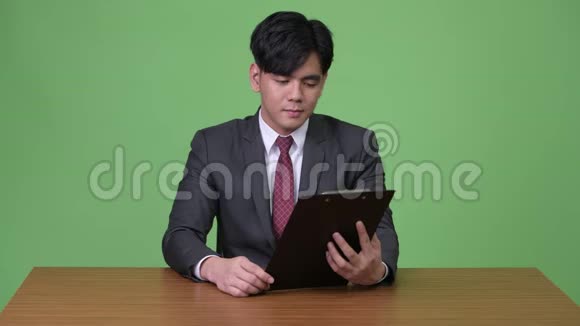年轻英俊的亚洲商人在绿色背景下工作剪贴板视频的预览图