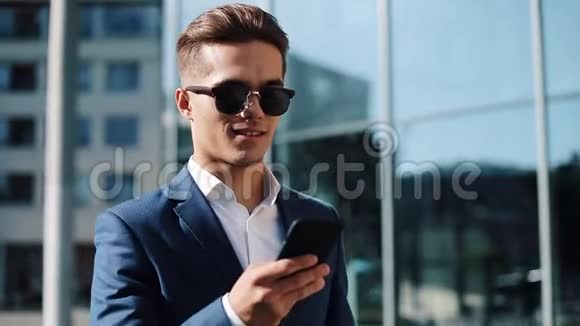 戴着太阳镜用智能手机在街上散步的年轻商人成功的生活商务风格旅行者视频的预览图
