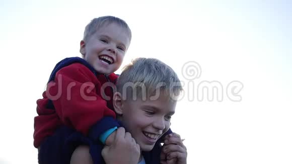 男孩拥抱他的弟弟把他抱在肩膀上孩子们欢声笑语日落视频的预览图