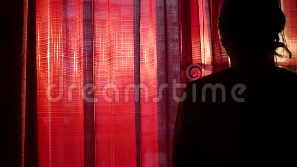 女孩打开红色的窗帘用手在阳光的光线下玩耍女孩的剪影视频的预览图