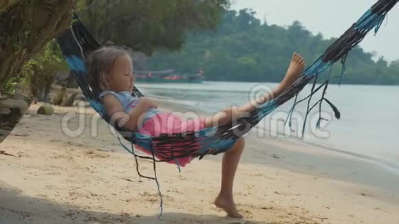 可爱的女孩躺在吊床上在沙滩上慢慢放松视频的预览图