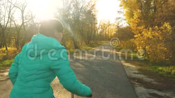 女孩骑自行车在秋天公园的沥青路上在黄树的背景下视频的预览图