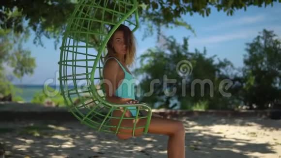 在前往热带岛屿的旅途中一位漂亮的年轻女性在吊椅上放松视频的预览图