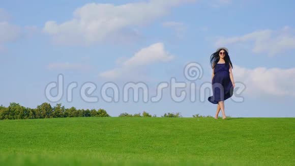 时髦的孕妇走在绿草上朝镜头走去视频的预览图
