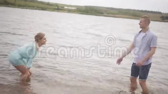 有爱心的夫妇在河岸上玩得很开心浪漫青春和蜜月快乐的男人和女孩在水里泼水视频的预览图