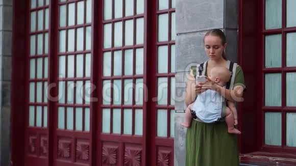 一位年轻的母亲抱着一个婴儿微笑着在她的智能手机上拍照走在街上视频的预览图