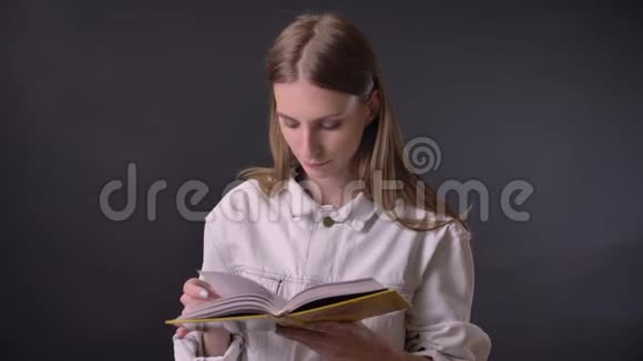 年轻可爱的女孩正在看书在镜头前看灰色背景视频的预览图