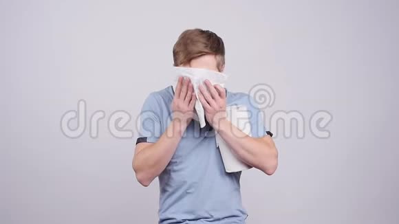 生病的年轻人用纸巾纸对着灰色背景吹鼻子视频的预览图