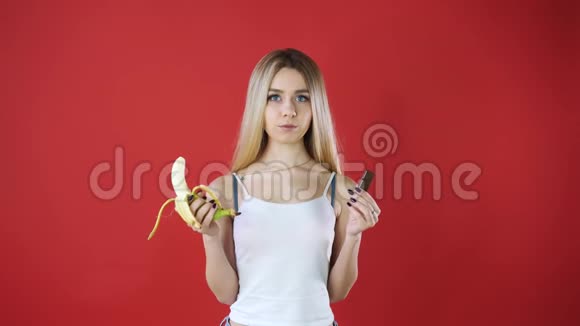 看有巧克力和香蕉的女人试图做出健康的选择控制她的体重隔离在红墙上视频的预览图