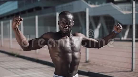 运动的非裔美国男人裸露的躯干摆姿势显示他的肌肉在户外在体育场附近摆姿势的黑人视频的预览图