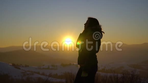 一个美丽的年轻女孩站在一座白雪覆盖的山上她把头发弄直了在背景下太阳落下视频的预览图